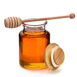 Honey in a glass jar with wooden dripper on top
